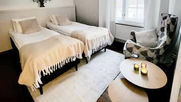 Een slaapkamer met twee eenpersoonsbedden, een stoel, een rond tafeltje met kaarsen en een wanddecoratie van een boom.