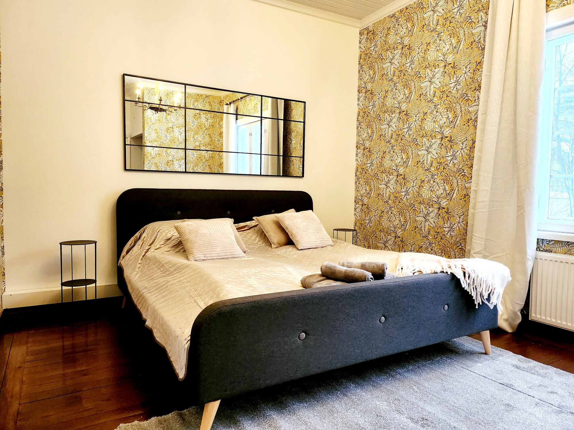A bedroom with a bed, a mirror, and a window with curtains.