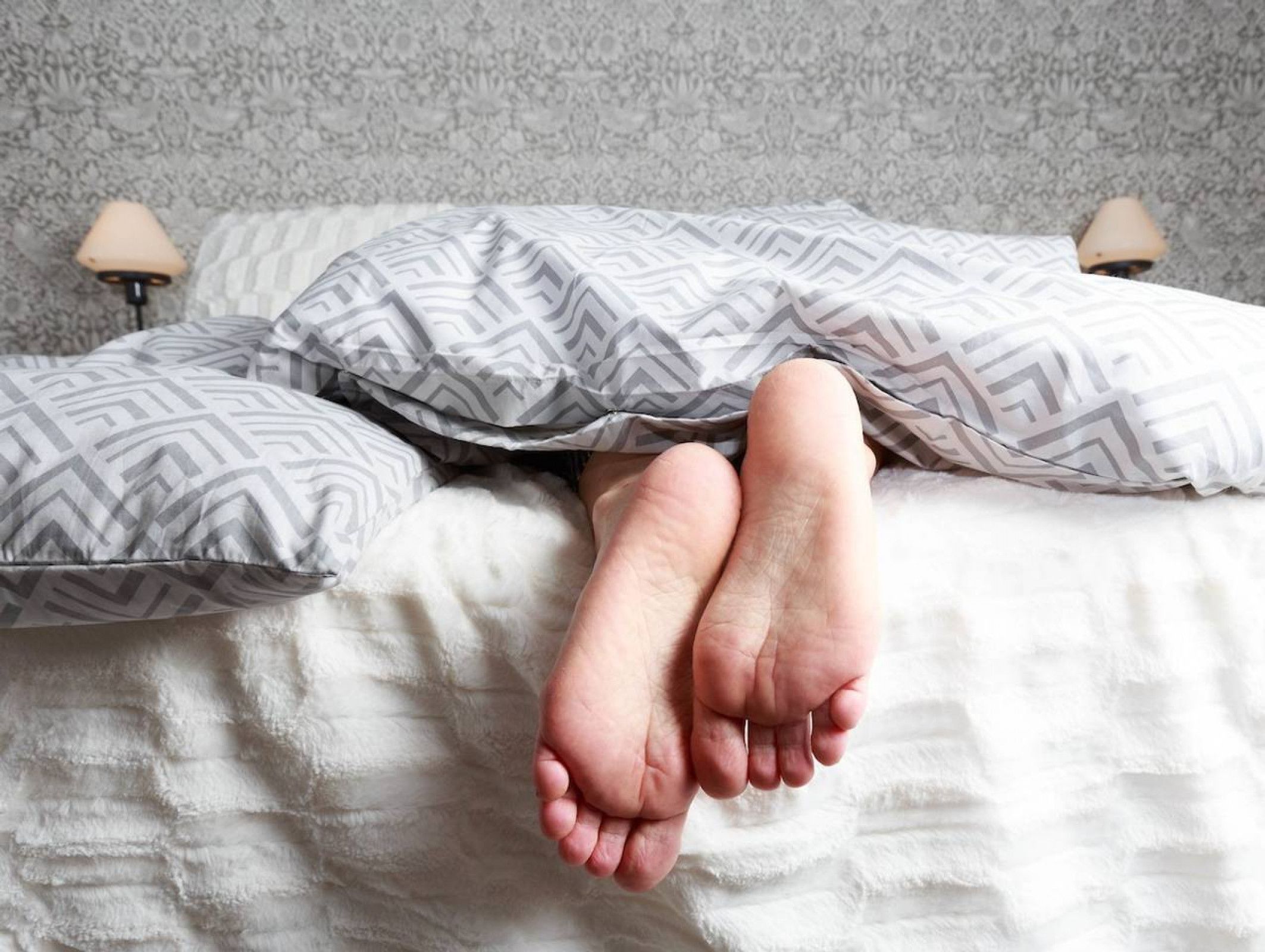 Una cama con almohadas estampadas y un edredón blanco liso.
