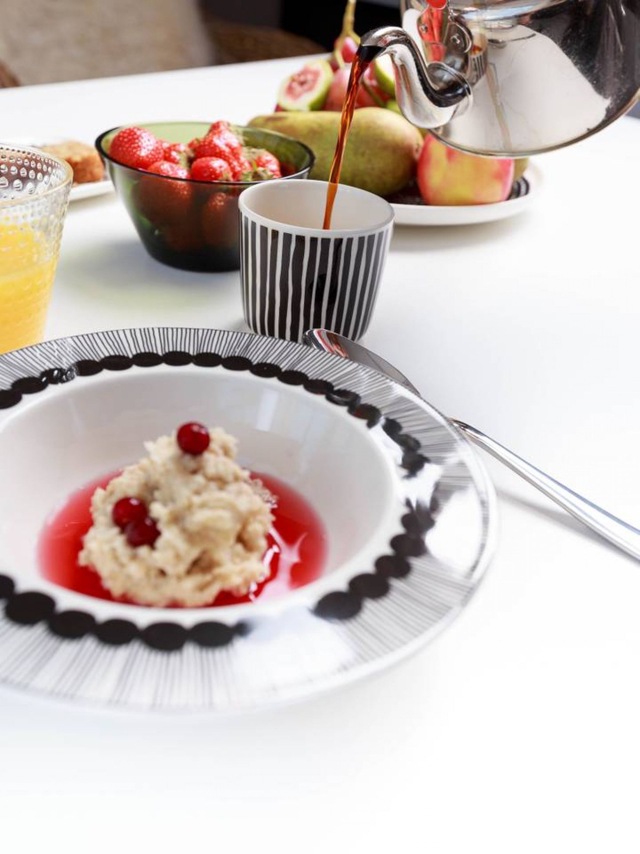 A breakfast setting with a bowl of oatmeal topped with red berries, a cup of coffee, and a glass of orange juice.