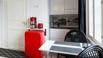 Een compacte keuken met witte kasten, een rode koelkast en een eethoek met een tafel en stoelen.