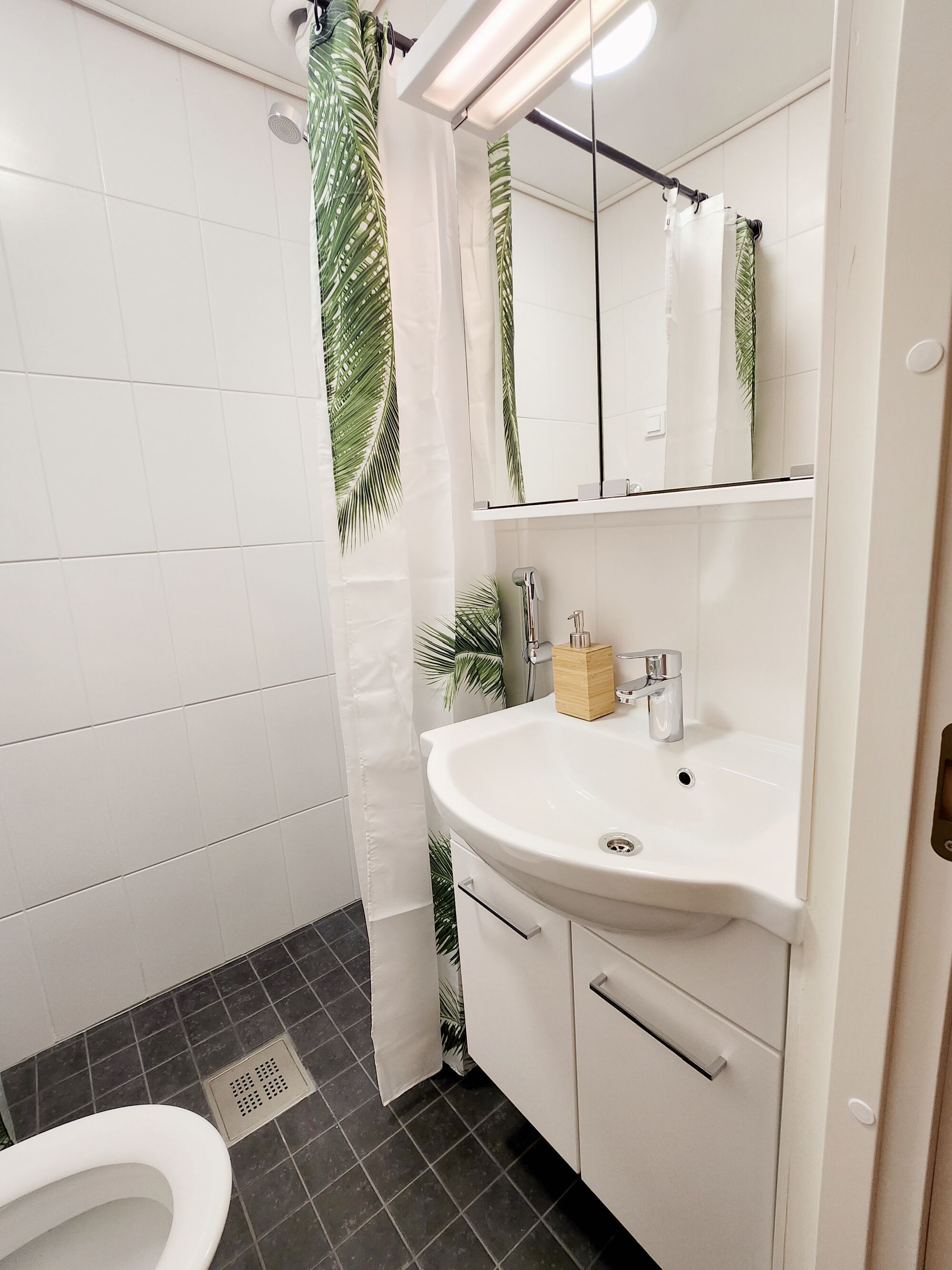 A bathroom with a white sink, mirror, and shower curtain with a palm leaf pattern.