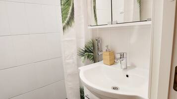 A bathroom with a white sink, mirror, and shower curtain with a palm leaf pattern.