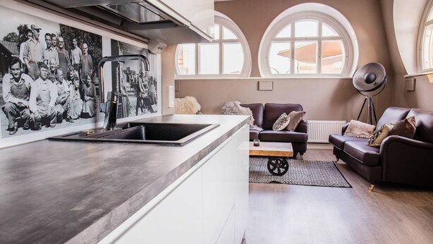 A modern kitchen with a large island, a dining area with a sofa and a coffee table, and a large window with arched tops. - Harmooni Suites (Jyväskylä)