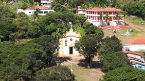 A white church with a bell tower, surrounded by lush greenery and residential buildings.