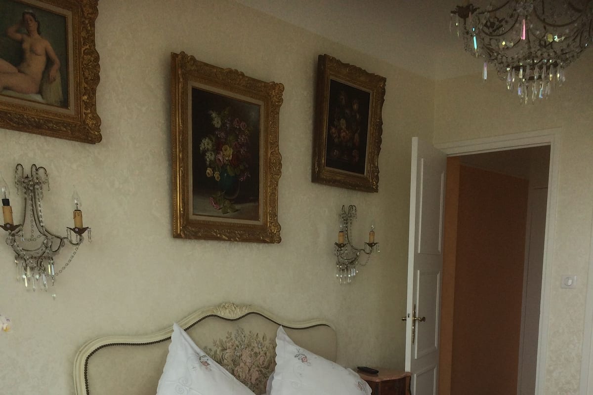 A neatly arranged bedroom with a bed, a wooden nightstand, a table with a tray of items, and a chair.