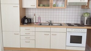 A compact kitchen with white cabinets, a stainless steel sink, a microwave, and a stove.