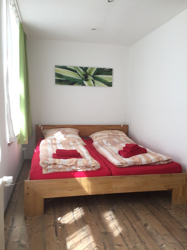 A single wooden bed with red bedding and a green plant on the wall. - Stadthaus Stralsund (Stralsund)
