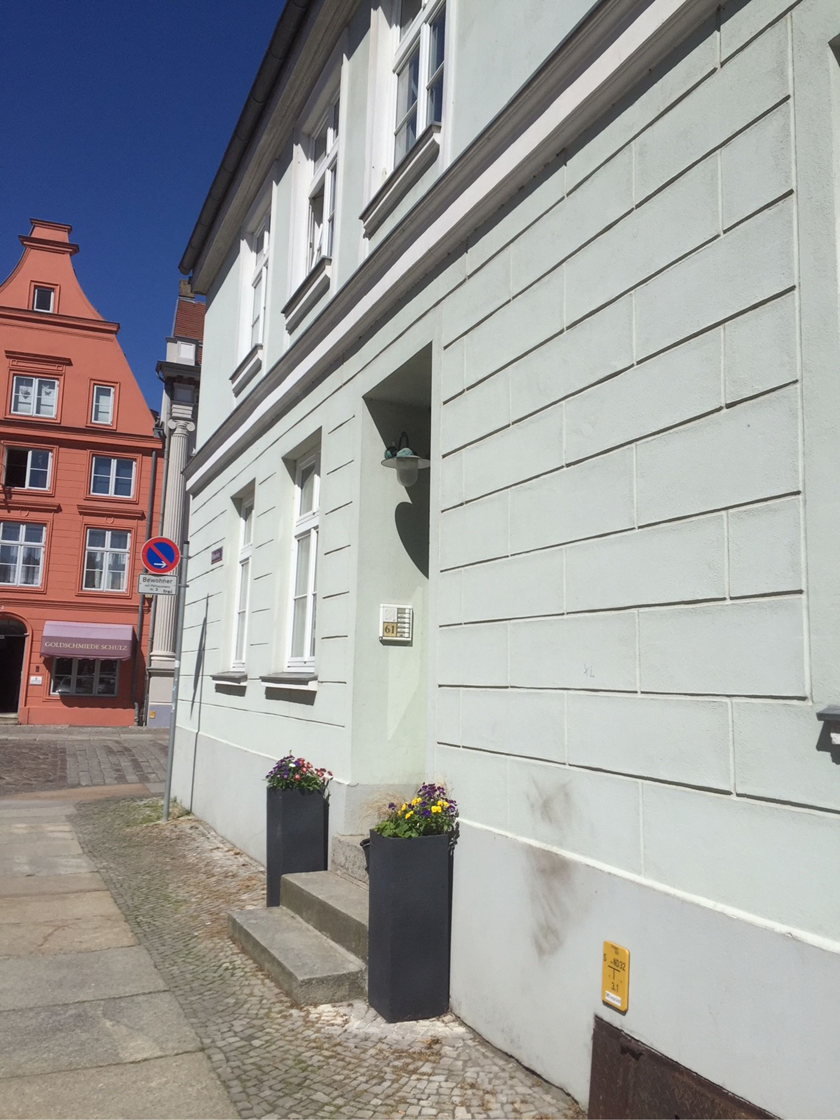 A white building with a red facade, a no parking sign, and flower pots on the sidewalk.