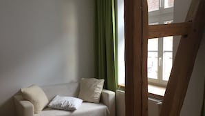 A room with a wooden floor, a white sofa with cushions, a green curtain, and a window with white frames.