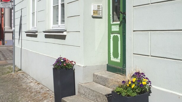 A building with a green door, white walls, and two flower planters on the steps.