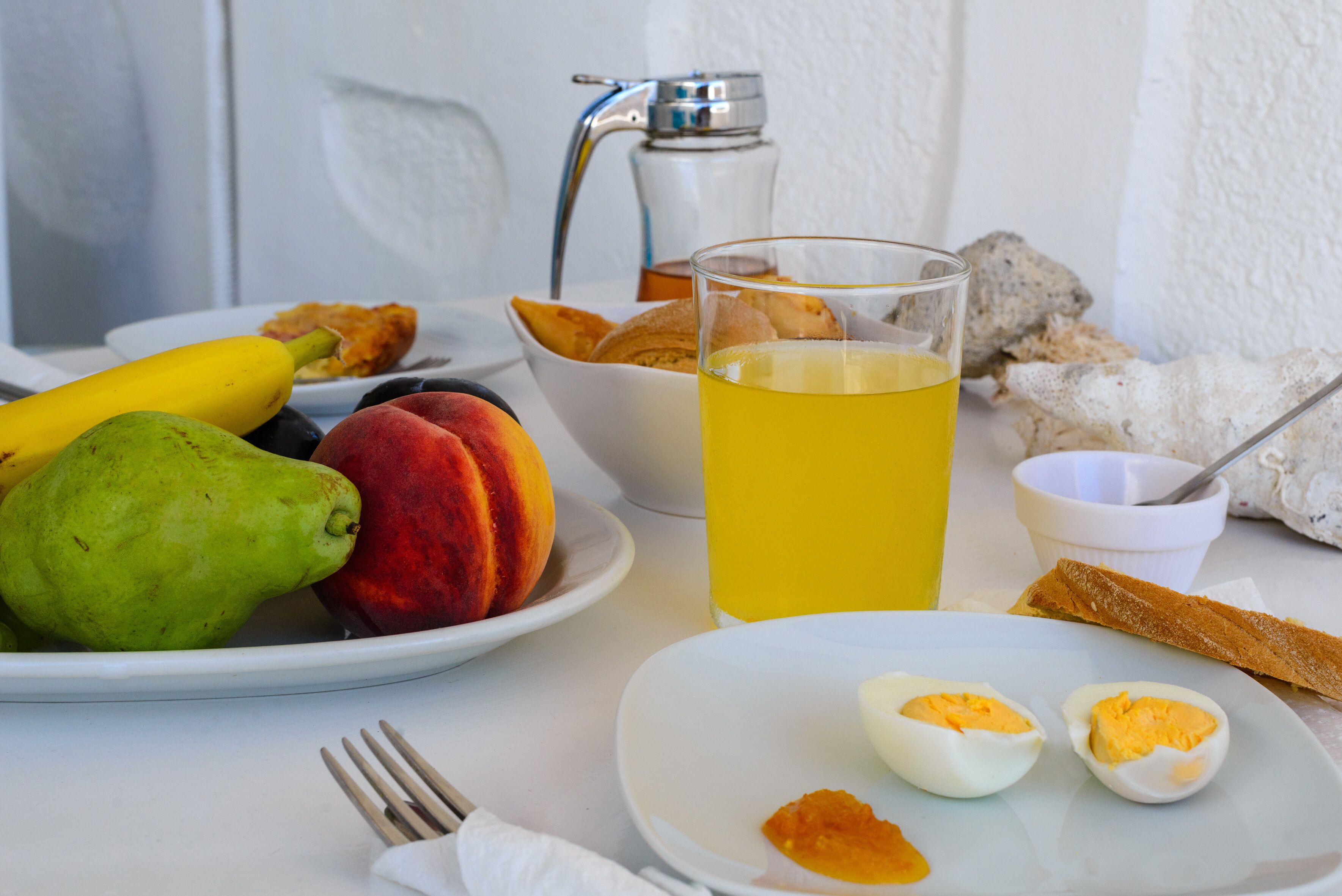 Une table dressée pour le petit-déjeuner, avec des fruits, des œufs, des toasts et un verre de jus.