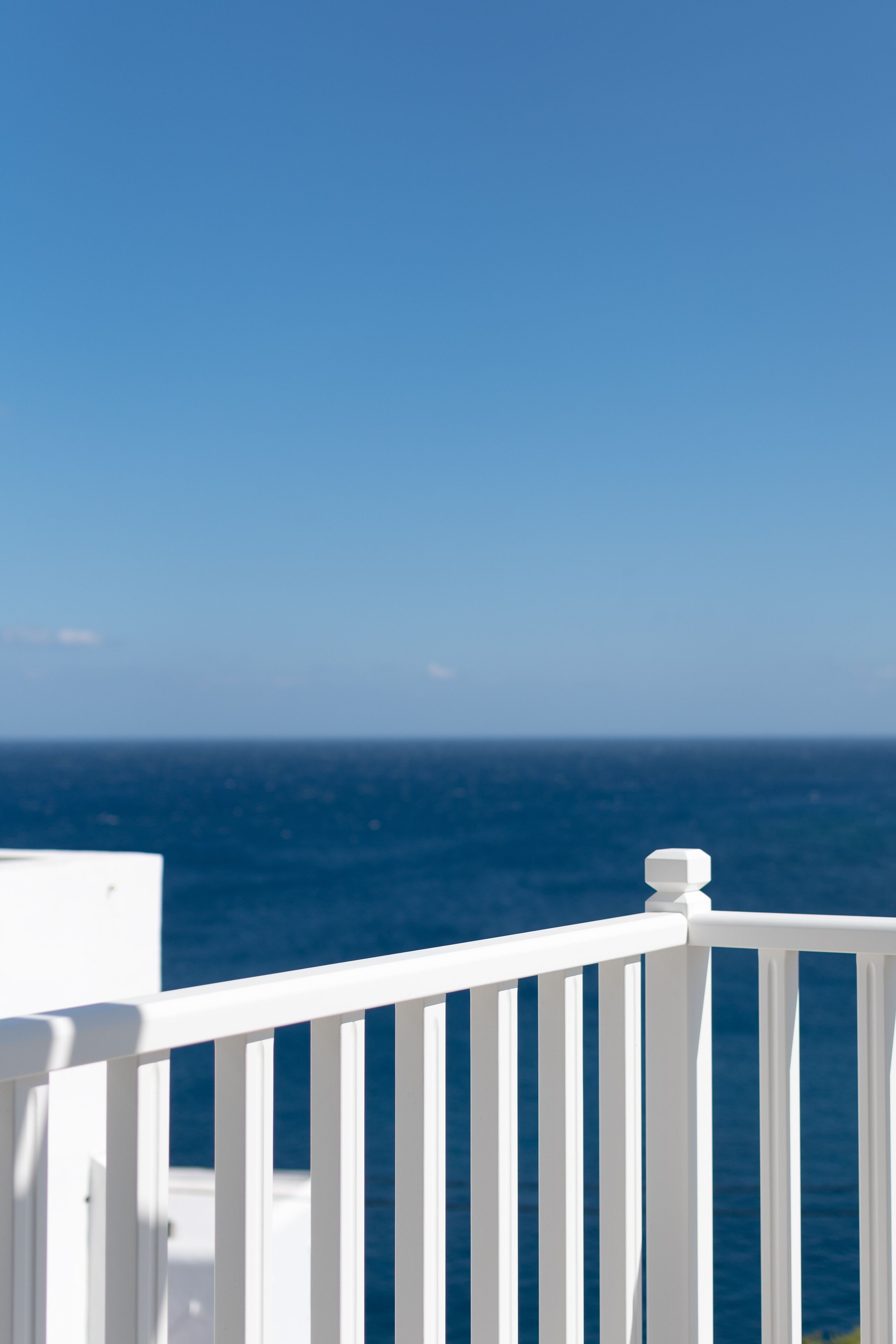 A white balcony railing overlooking a clear blue sea.