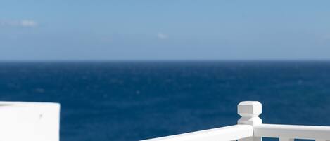 A white balcony railing overlooking a clear blue sea.