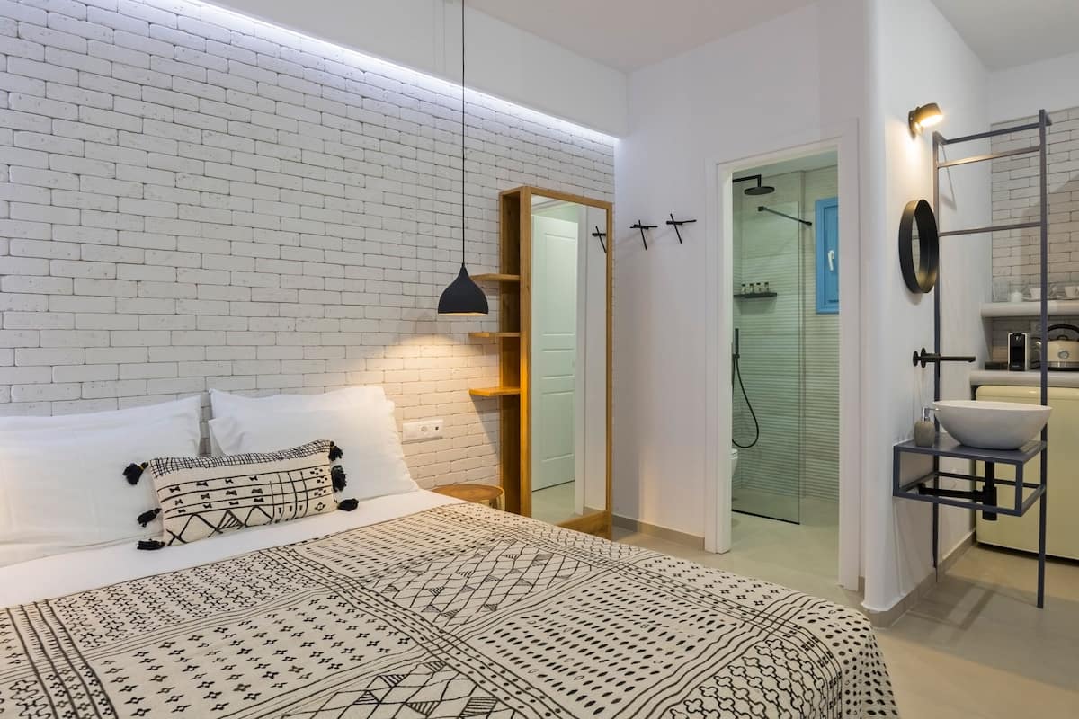 Une chambre moderne avec un mur en briques, un lit avec une literie à motifs, une lampe de chevet, un miroir et un dressing avec une douche.