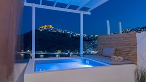 A modern outdoor pool area with a view of a cityscape and a hill in the background. - Ihthioessa Boutique Hotel (Astypalaia)