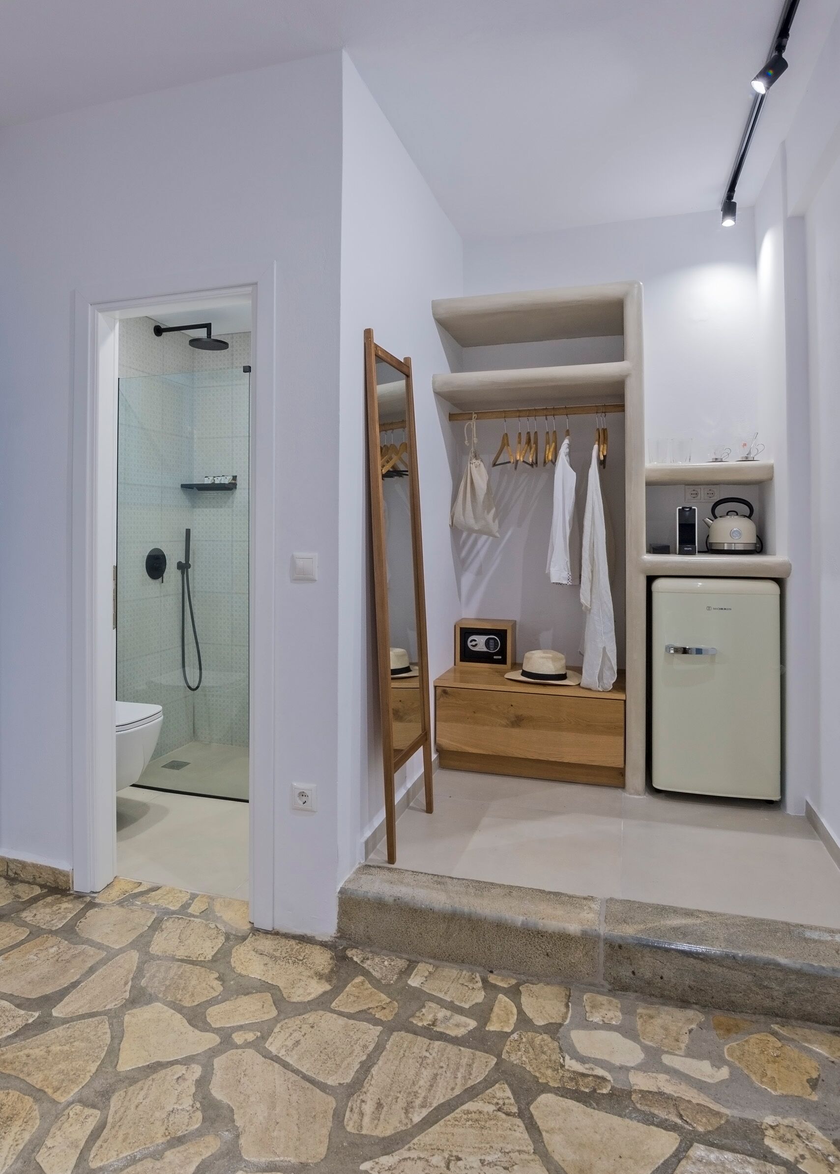 A bathroom with a glass shower enclosure, a wooden vanity with a radio, and a small refrigerator.