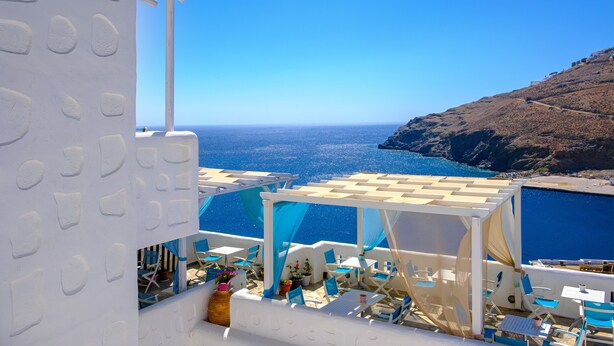 A terrace with white walls and blue accents, overlooking a clear blue sea and a rocky coastline. - Ihthioessa Boutique Hotel (Astypalaia)