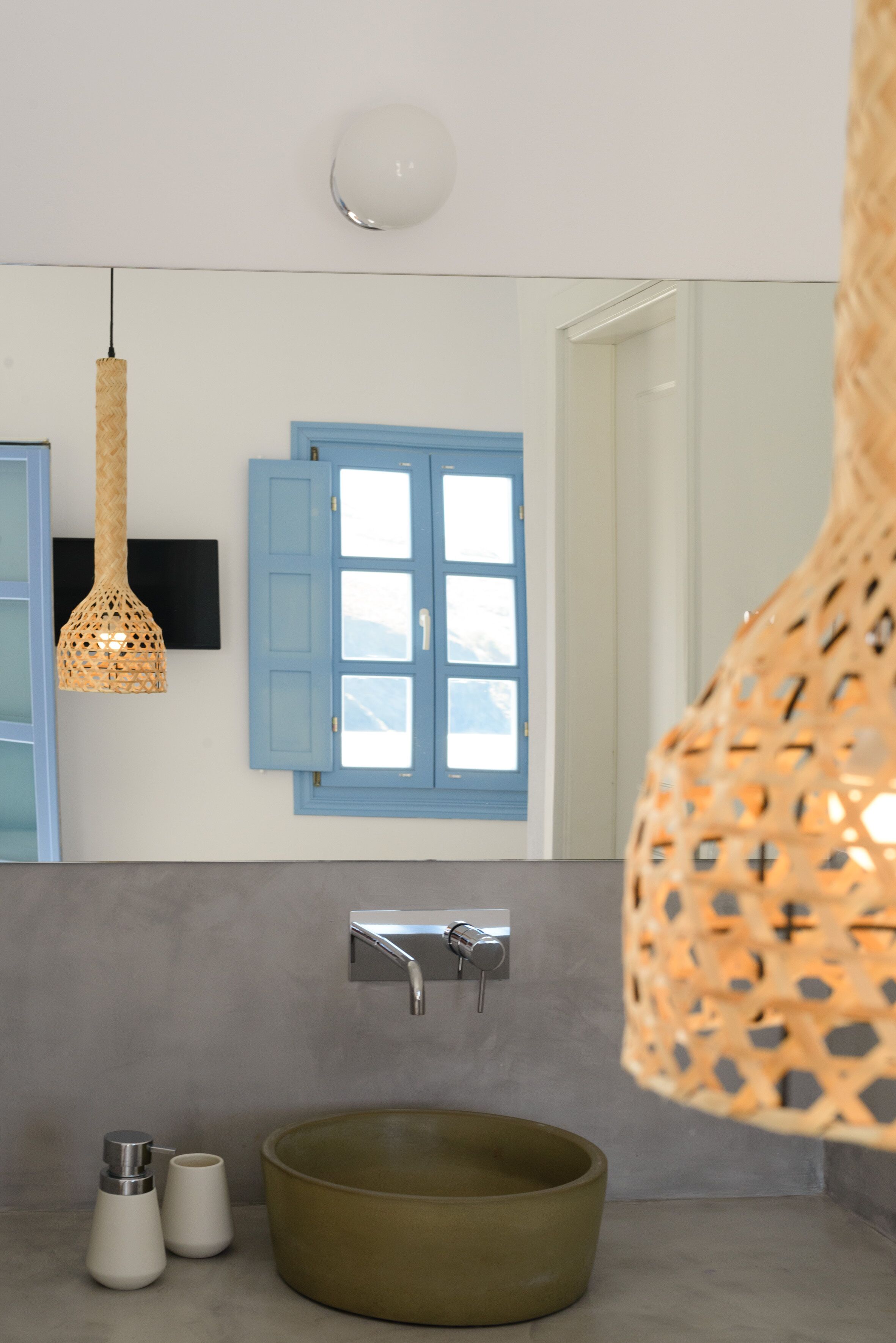 Un baño con un lavamanos redondo, una ventana azul y una lámpara colgante.