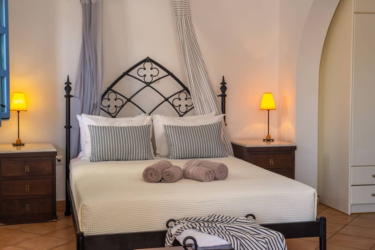Un lit bien fait, agrémenté d’oreillers à rayures, une tête de lit à motifs losangés et deux lampes de chevet.
