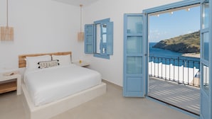 A bedroom with a bed, bedside table, and a view of the sea through an open door. - Ihthioessa Boutique Hotel (Astypalaia)