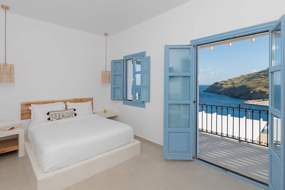 Une chambre à coucher avec un lit, une table de chevet et une vue sur la mer, visible à travers une porte ouverte.