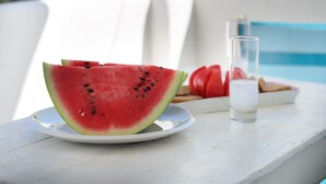 Una mesa con una fuente de sandía en rodajas, un vaso de agua y un plato de pan y tomates.