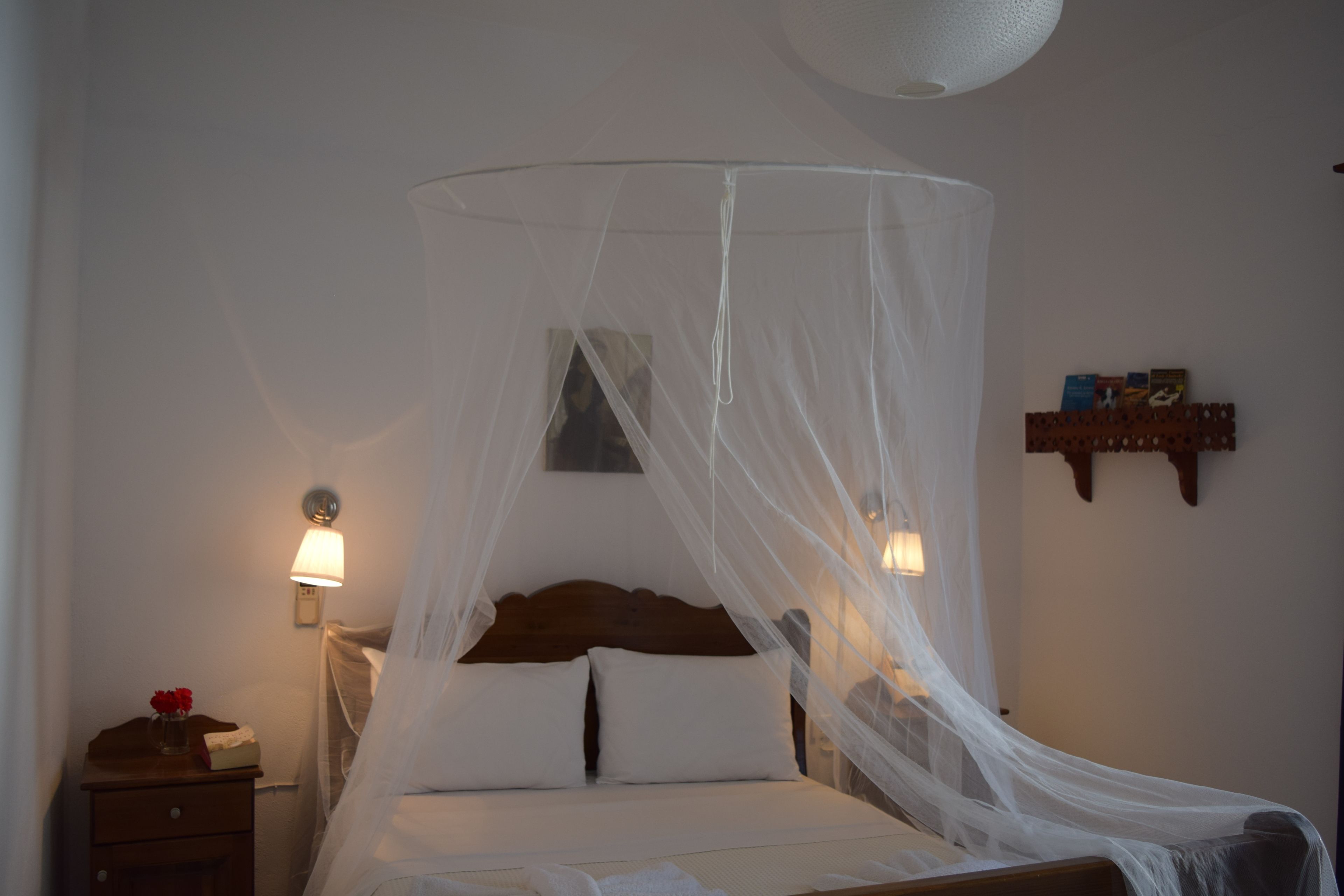 A bed with a canopy, bedside lamps, a nightstand, and a small shelf with books.