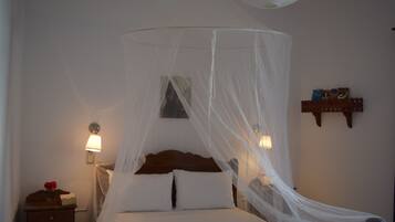 A bed with a canopy, bedside lamps, a nightstand, and a small shelf with books.
