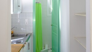Un pasillo estrecho con una zona de cocina a la izquierda, una puerta verde al final y un arco blanco arriba.