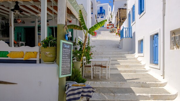 Una calle estrecha con edificios blancos y puertas azules, que sube un tramo de escalones de piedra.