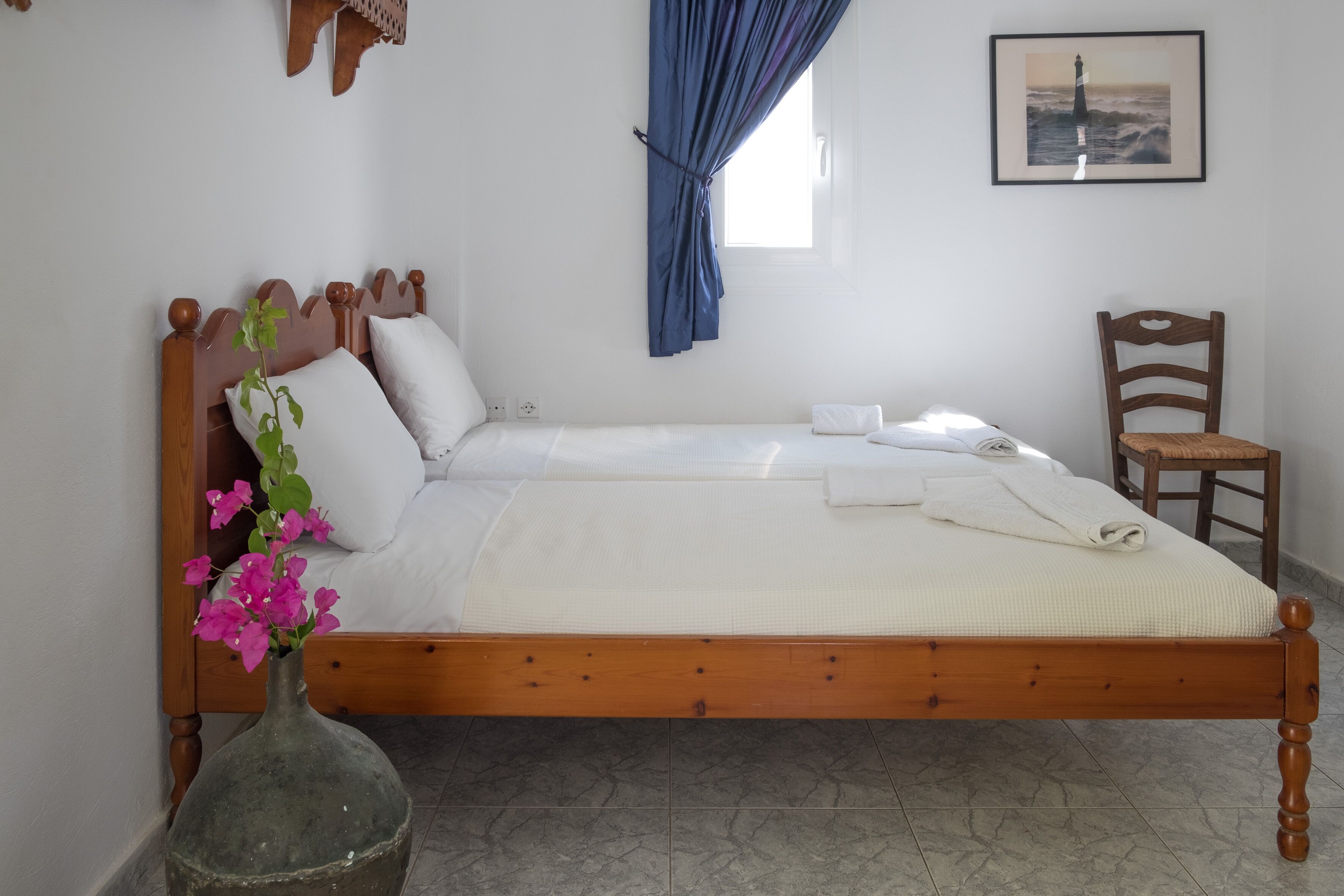 Un lit bien fait, avec du linge de lit blanc, une tête de lit en bois et un vase rempli de fleurs roses.
