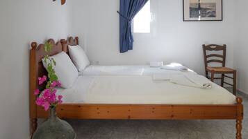 Un lit bien fait, avec du linge de lit blanc, une tête de lit en bois et un vase rempli de fleurs roses.