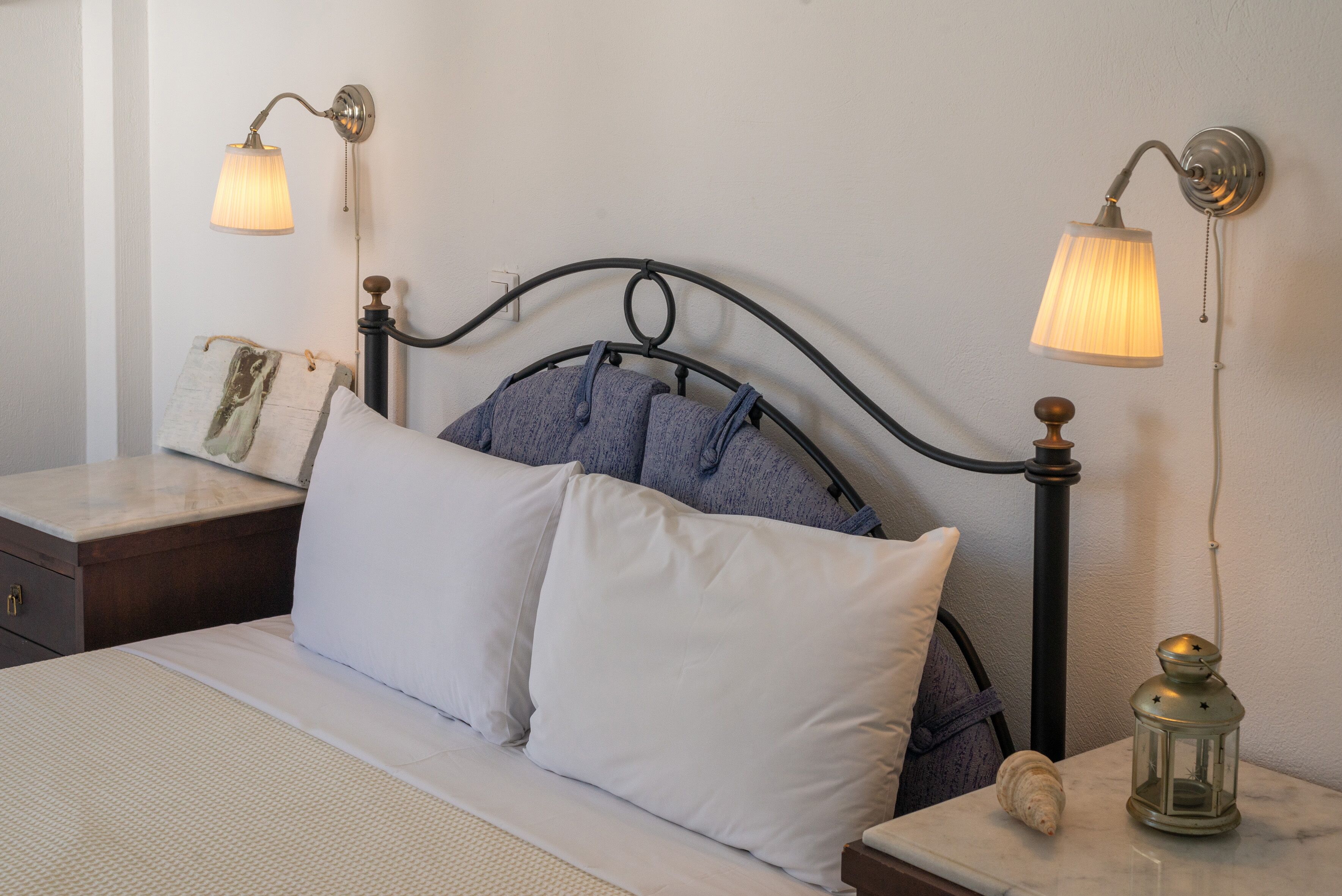 A neatly made bed with white linens, a headboard with a curved design, and two wall-mounted lamps.
