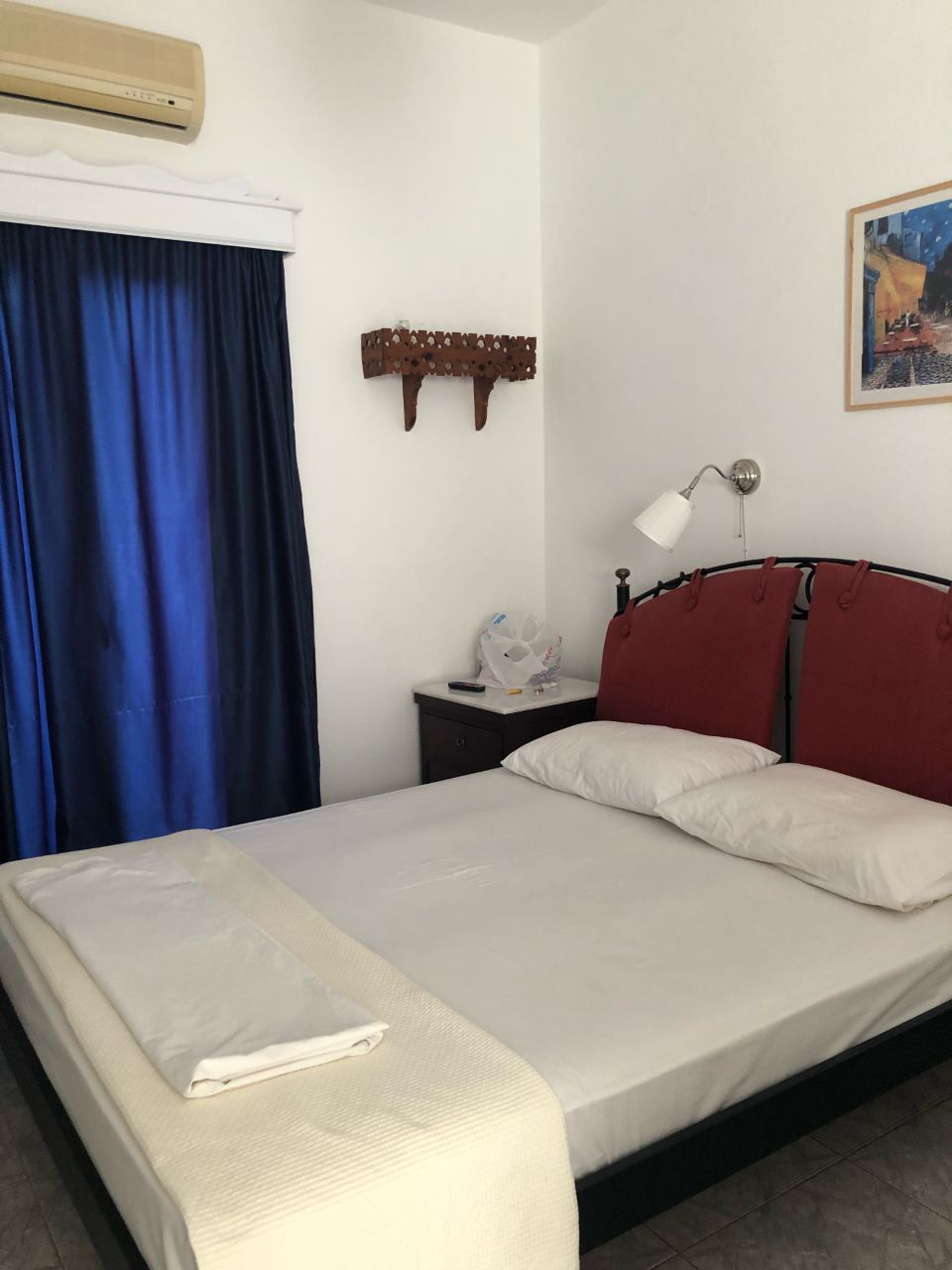 Habitació d'hotel amb un llit, una tauleta de nit, una làmpada, aire condicionat fixat a la paret i un quadre.