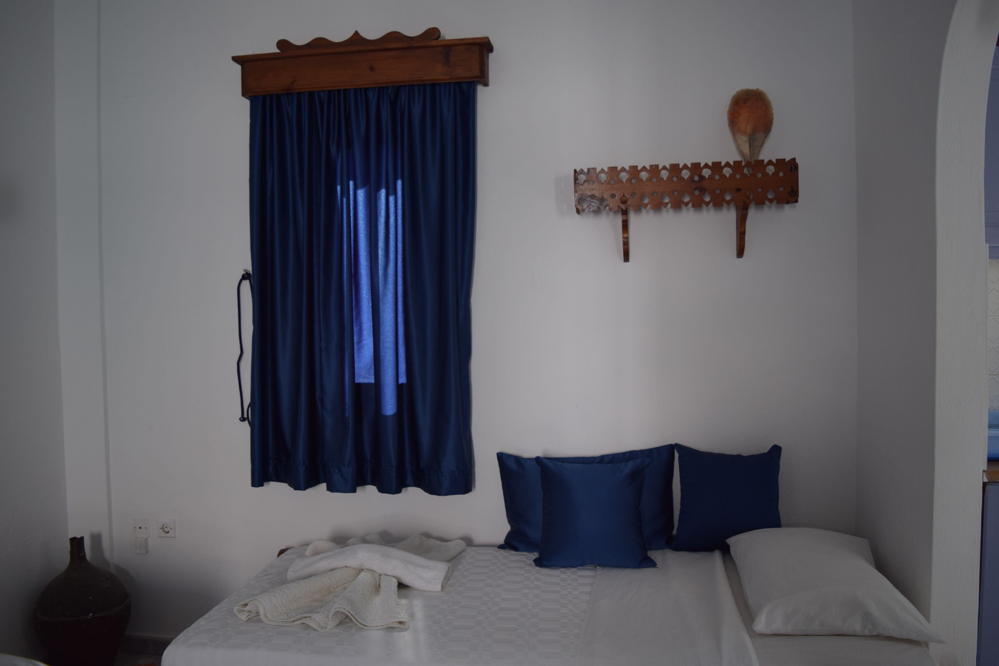 Une chambre à coucher avec un lit, des rideaux bleus, un objet décoratif fixé au mur et un vase posé sur une table de chevet.