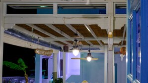 Un restaurante con mesas y sillas blancas, techo de madera y vista al cielo nocturno.