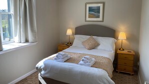 A neatly made bed with white linens and two bedside lamps, a window with curtains, and a framed picture on the wall. - Kilmartin Hotel (Lochgilphead)