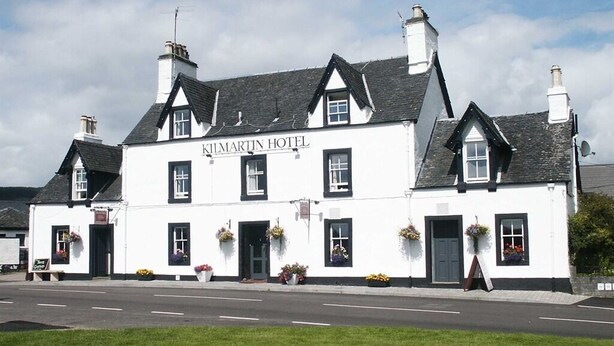 A traditional white building with the sign "Kilmartin Hotel" on the front. It has multiple chimneys, black-framed windows, and flower baskets hanging from the windows. - Kilmartin Hotel (Lochgilphead)