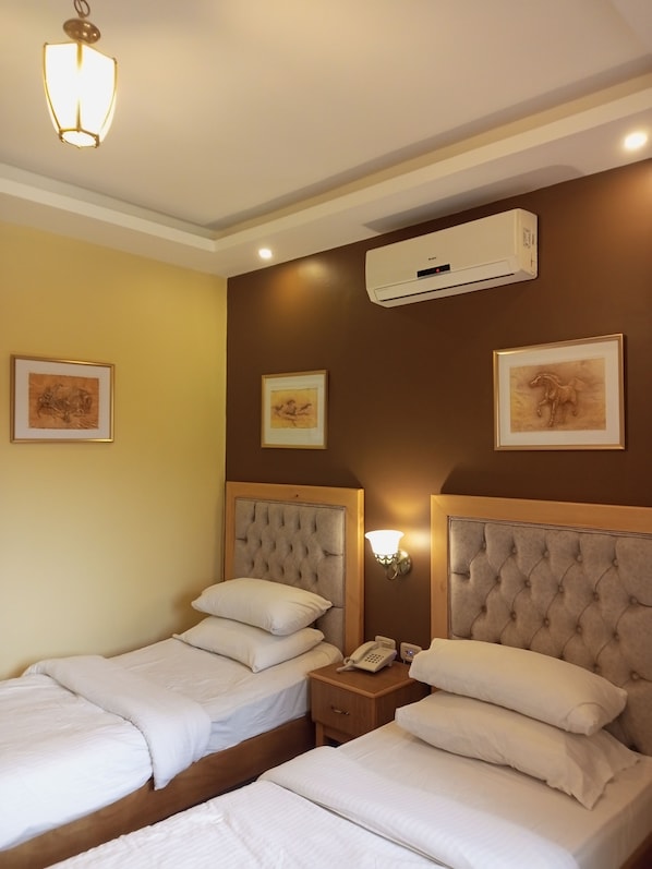A hotel room with two beds, a bedside telephone, and wall-mounted air conditioning.
