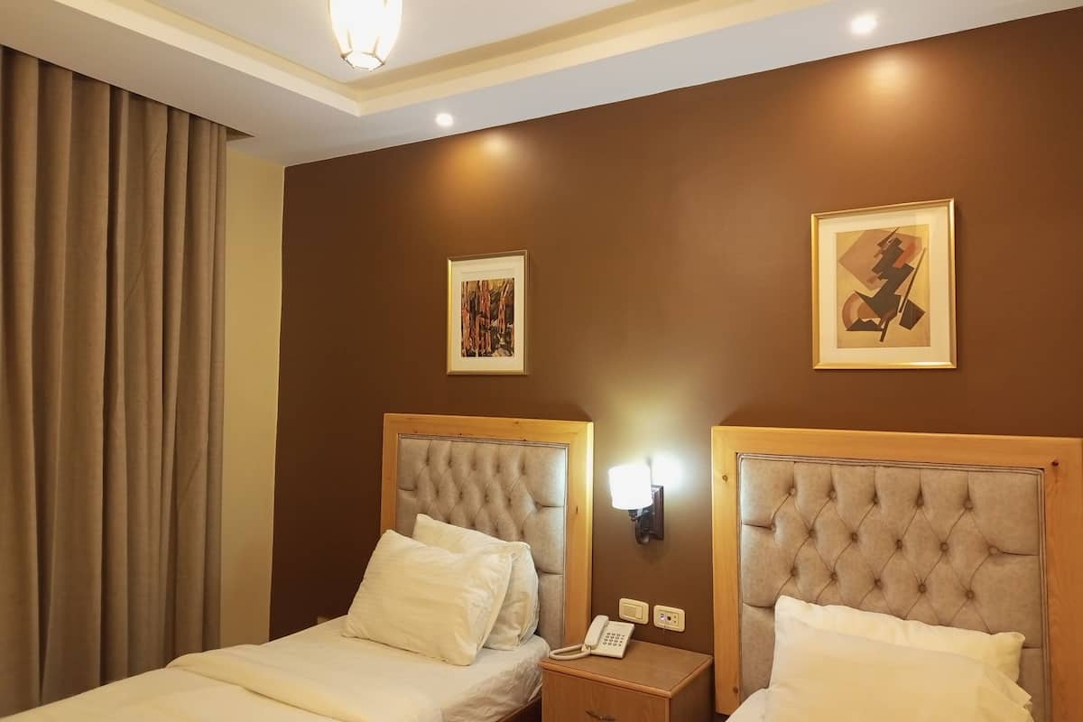 A hotel room with two beds, a nightstand with a phone, and two framed pictures on the wall.