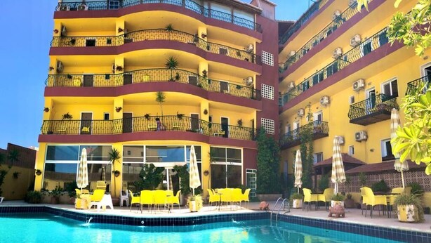 Un hotel de varios pisos con balcones, piscina y mobiliario exterior.