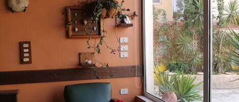 Interior de un restaurante con una mesa, sillas, plantas colgantes y vistas al exterior.