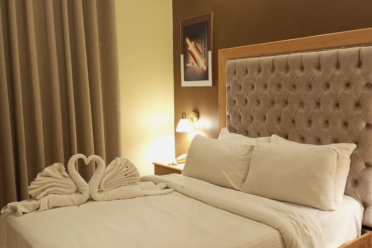 A hotel room with a large bed, a headboard, a nightstand, a lamp, and a framed picture on the wall.