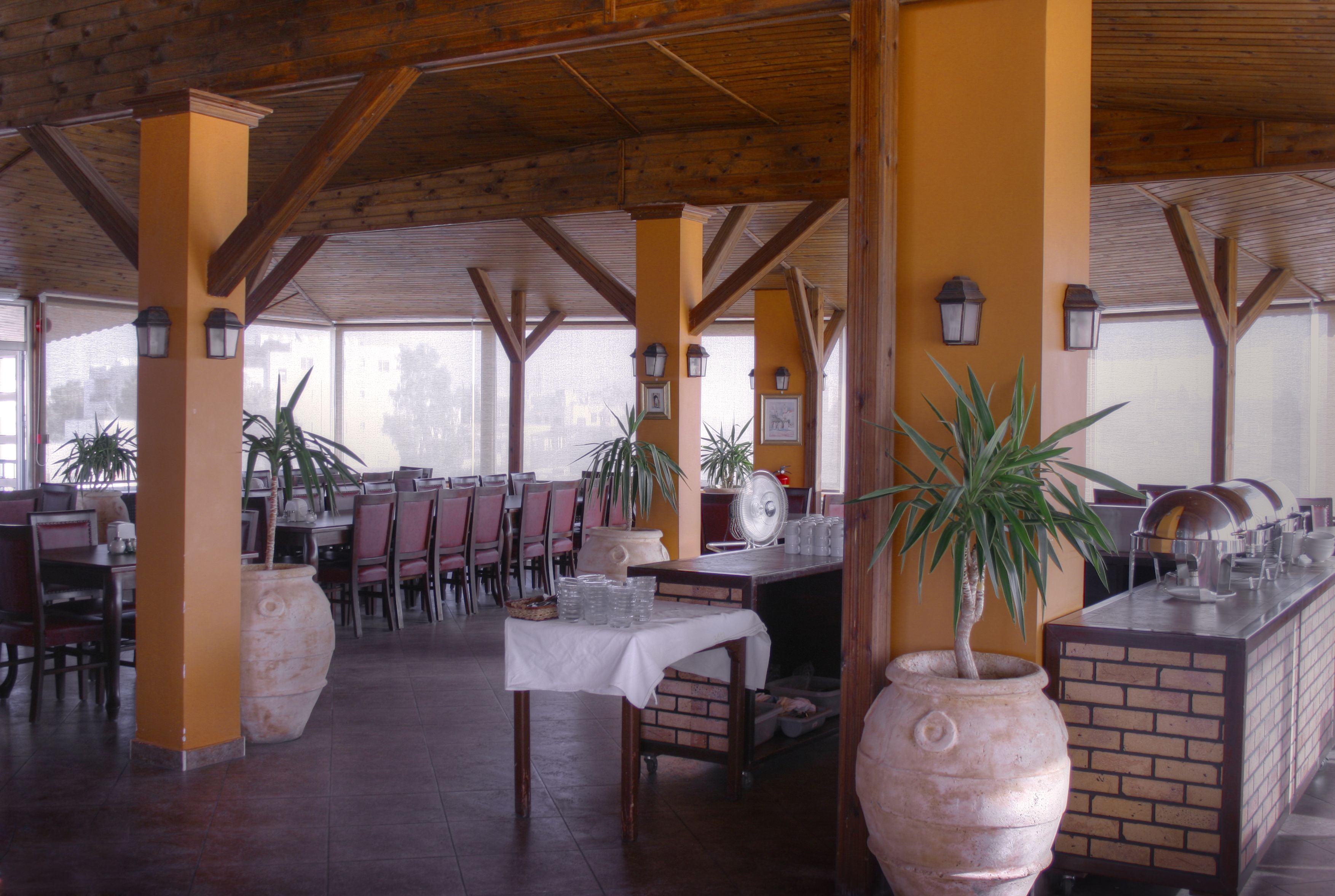 A restaurant with wooden beams, brick walls, and large potted plants. Tables are set with white tablecloths and glassware.