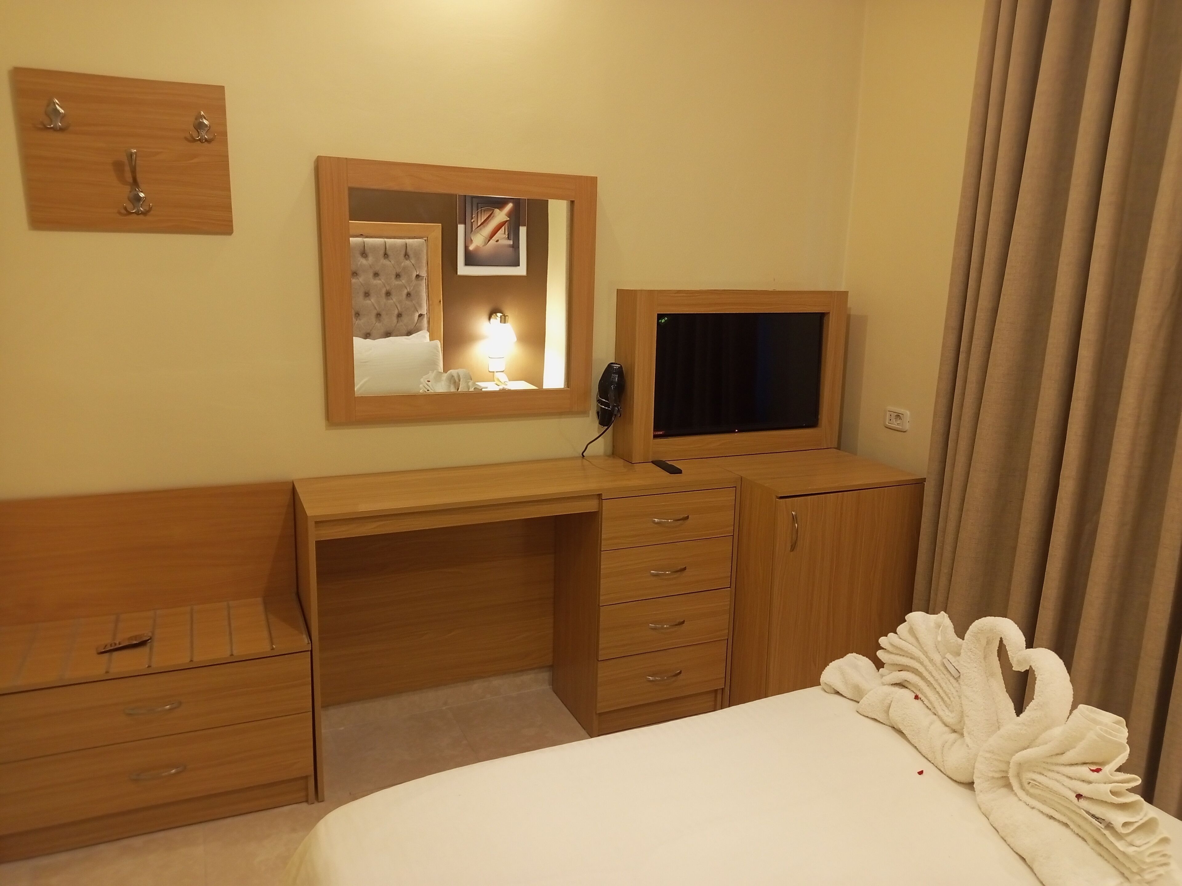 Una habitación de hotel con un escritorio de madera, una cama, un televisor, un espejo y una bata.