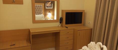 Una habitación de hotel con un escritorio de madera, una cama, un televisor, un espejo y una bata.