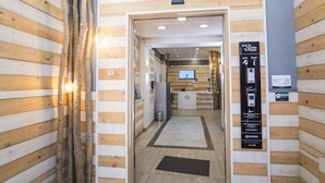 Zona de recepción de un hotel con paneles de madera, un mostrador de recepción, una pantalla digital y un cartel con información de contacto.