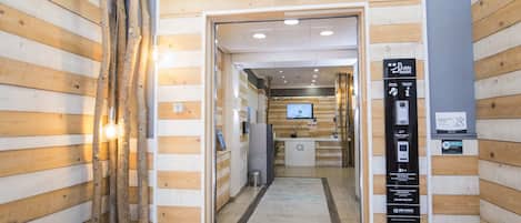 Zona de recepción de un hotel con paneles de madera, un mostrador de recepción, una pantalla digital y un cartel con información de contacto.
