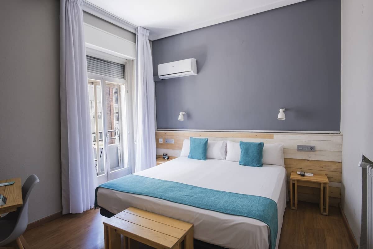 Ein Hotelzimmer mit Bett, Nachttischen, Schreibtisch und einem Fenster mit Vorhängen.